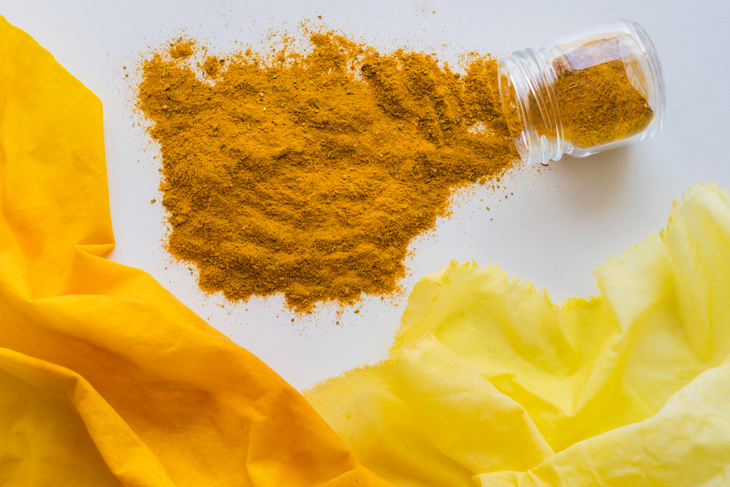 Turmeric powder spilled from a glass jar - natural skincare ingredient for glowing melanin-rich skin