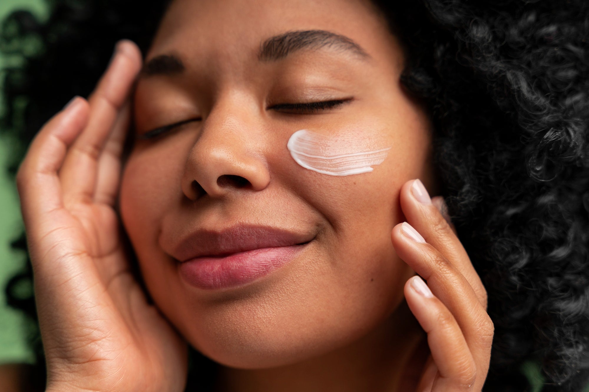 Black woman applying skincare cream for glowing melanin-rich skin - Charlene Beauté skincare routine
