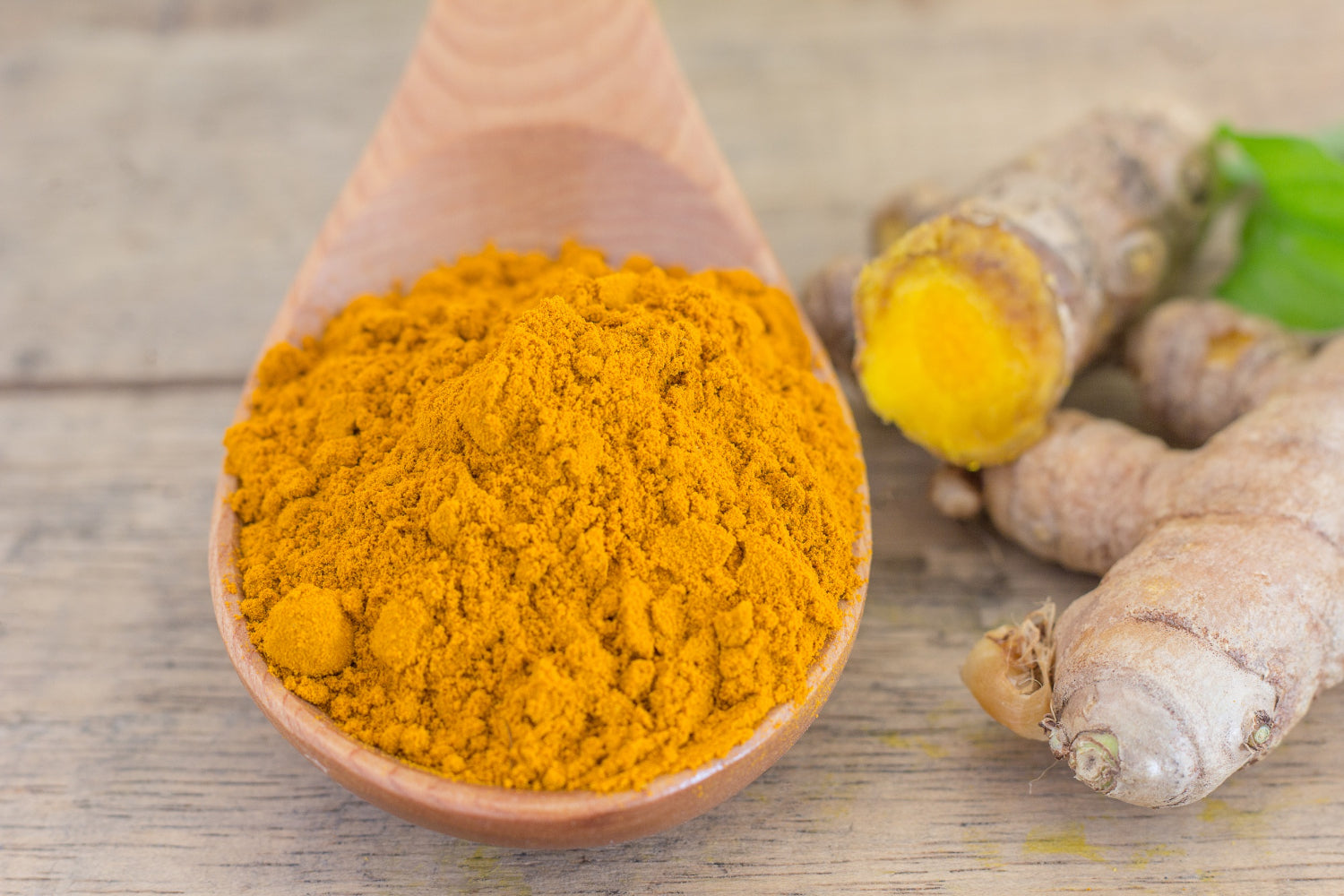 Fresh turmeric root and powder on wooden spoon - natural brightening ingredient for melanin-rich skincare